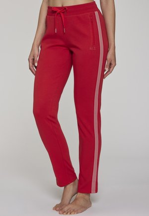 Red slim-fit sweatpants with white side stripes, zippered pocket on right thigh, and drawstring waist, worn barefoot by a standing person.