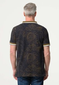 Zwart poloshirt met korte mouwen en een gouden abstract patroon, contrasterende witte en gouden kraag en manchetten. Zachte textuur, perfecte pasvorm.