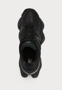 Baskets de sport noires avec une tige texturée, dotées d'une pointe arrondie, de lacets plats et d'un accent argenté à la base. Design simple et épuré.
