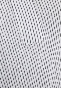 Gros plan sur un tissu blanc avec de fines rayures noires verticales et un détail de couture.