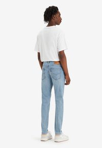 Blå jeans med straight-leg passform, lys vask, baklommer og merket lærlapp, kombinert med en enkel hvit t-skjorte og hvite sneakers.