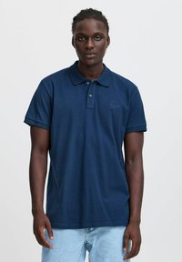 Temno modra polo majica iz bombaža, z nadlahti, ovratnikom z gumbnim zapiranjem in majhnim vezenim logotipom na prsih.