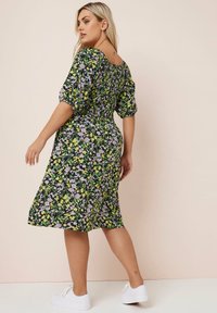 Kukkamekko, jossa on musta tausta ja keltaisia sekä violetin kukkia. Rypytetty yläosa, puffihihat ja polven pituinen helma. Valkoiset lenkkarit.