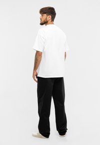 Bílá bavlněná trička s volným střihem, spárovaná s černými volnými kalhotami a béžovými teniskami. Má krátké rukávy a design s kulatým výstřihem.