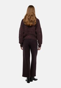Pull en tricot épais dans des tons rouge foncé et violet, associé à un pantalon à larges jambes en tartan dans des teintes sombres, porté avec des bottines noires.