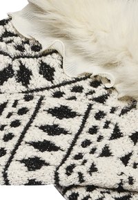 Mustavalkoinen kudottu kangas, jossa on geometrinen kuvio, pehmeä tekstuuri ja pörröinen valkoinen korostus reunassa.