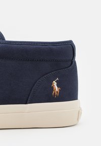 Canvas sneakers i marinblått med en ljusbrun gummisula. Utrustad med en broderad polo-spelare logotyp på hälen. Slät textur, enkel design.