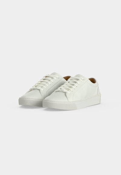 Λευκά δερμάτινα sneakers χαμηλού προφίλ με κορδόνια, στρογγυλεμένες μύτες και επίπεδες λαστιχένιες σόλες σε απλό λευκό φόντο.