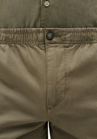 Pantaloni verde măsliniu cu închidere prin buton, talie elastică și textură netedă, având detalii subtile de cusătură pe material.
