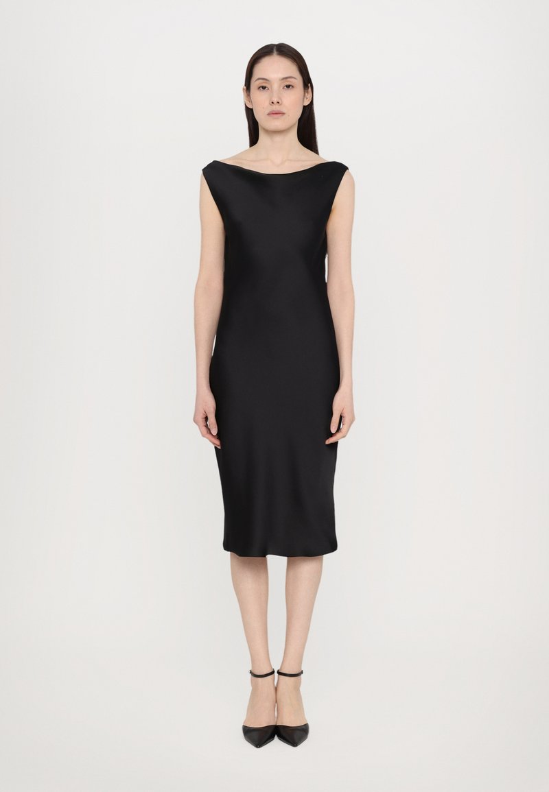 Vestido midi de satén negro con escote barco, diseño sin mangas y textura suave. Combinado con tacones negros de punta fina. Silueta minimalista.
