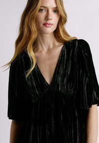 Robe en velours noir avec un décolleté en V profond, des manches courtes bouffantes et des plis verticaux, créant une apparence texturée et élégante.