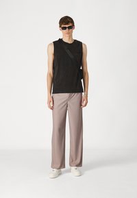 Un débardeur noir sans manches, un pantalon à rayures brun clair et des baskets blanches. Les accessoires comprennent des lunettes de soleil noires fines et un sac bandoulière noir.