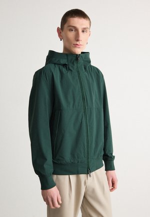 Chaqueta verde con capucha, cierre de cremallera, puños y cintura elásticos, fabricada en material ligero. Textura suave, diseño minimalista.