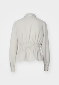 Lys beige langermet bluse med krage og elastisk midje. Glatt tekstur med samlet detaljer i midjen.