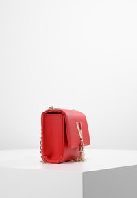 Borsa a tracolla rossa in pelle sintetica con chiusura a patta, hardware dorato e tracolla a catena. Superficie testurizzata e forma rettangolare compatta.
