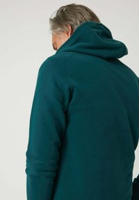 Sudadera con capucha color azul verdoso con textura suave, con escote redondo y capucha grande, vista desde atrás, mostrando detalles de costura simples.