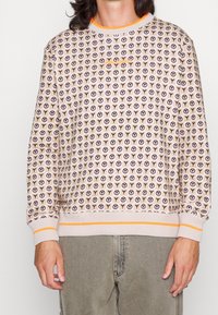 Maglione realizzato in morbido tessuto, con uno sfondo beige chiaro e un motivo a logo ripetuto in marrone e arancione. Polsini a coste con accenti arancioni.