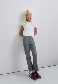 Camiseta blanca de corte cropped con un pequeño logo, combinada con pantalones grises con un patrón de estampado de leopardo en rosa y zapatillas oscuras moradas.