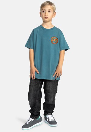 Teal oversized t-shirt met cirkelvormig logo, zwarte jeans en grijze sneakers met teal accenten. Eenvoudig ontwerp en casual pasvorm.