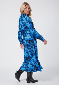 Sukienka z długim rękawem w kolorze granatowym, z jasnoniebieskim wzorem kwiatowym. Płynna sylwetka, materiał o delikatnym połysku, zestawiona z czarnymi kowbojkami.