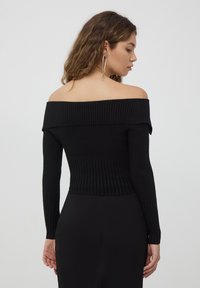 Top nero a coste con spalle scoperte, maniche lunghe, lunghezza cropped e tessuto testurizzato. Modello mostrato da dietro, abbinato a una gonna nera.