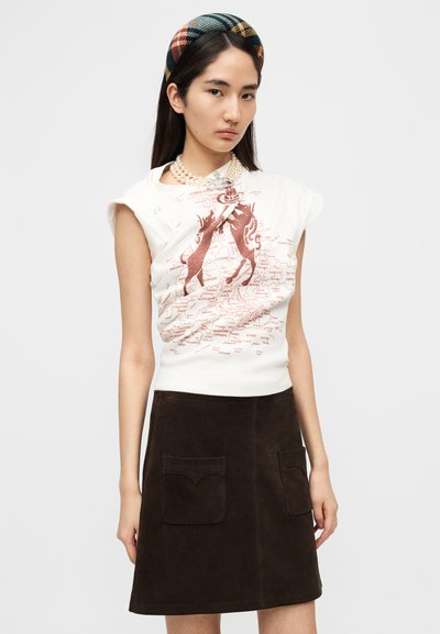 Λευκό αμάνικο τοπ με κόκκινο γραφικό σχέδιο. Καφέ σουέντ φούστα σε στυλ Α γραμμής με δύο μπροστινές τσέπες. Μοντέλο φοράει καρό κορδέλα και μαργαριτάρια.