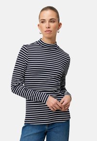 Dlhý rukávový top s námorníckymi modrými a bielymi pruhmi, s vysokým golierom a priliehavým strihom, vyrobený z jemnej látky. Kombinovaný s modrými džínami.