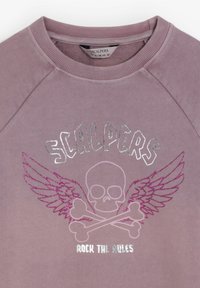 Sudadera morada con un gráfico en relieve de una calavera con alas y huesos cruzados, acentuada con texto brillante en plateado y rosa.