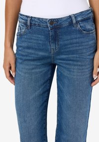 Blugi din denim într-o nuanță medie de albastru, având un design clasic cu cinci buzunare, estompare subtilă și închidere cu nasture în față.