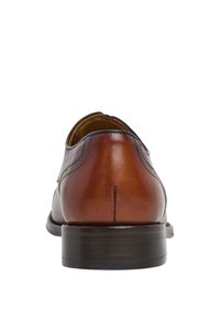 Zapato de cuero marrón con un acabado suave, parte trasera redondeada y acentos negros contrastantes. La suela es plana y presenta una textura sutil.