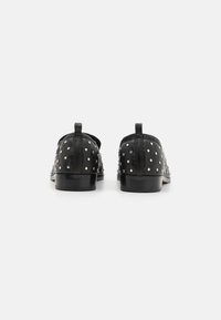 Black leather shoes featuring a rounded toe, small metal studs across the upper, and a low heel. Includes a loop tab on the heel.
