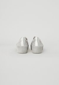 Zapatillas metálicas plateadas con suela plataforma, textura suave y diseño de punta redonda. La vista trasera muestra suela acanalada y detalles de costura.