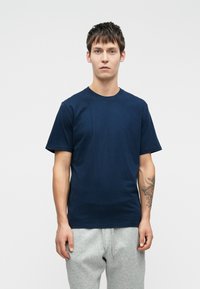 Camiseta de algodón azul marino de manga corta y cuello redondo, combinada con pantalones de chándal grises. La textura parece suave y sin adornos.