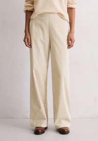 Cremfarbene Cordhose mit weitem Bein, einer gerippten Textur und elastischem Bund, kombiniert mit braunen Leder-Ankle-Boots.