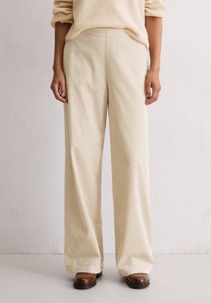 Pantalons larges en velours côtelé crème avec une texture ribbelée et une taille élastique, associés à des bottines en cuir marron.