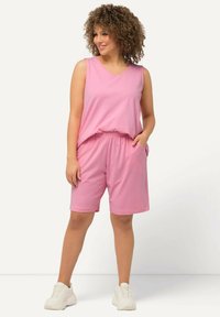 Top rosa senza maniche con scollatura a V e pantaloni corti coordinati con vita elastica. Entrambi realizzati in tessuto morbido e leggero. Sneakers bianche.