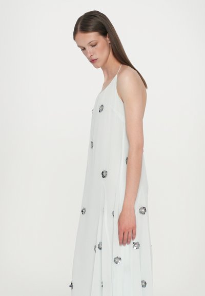 Vestido blanco, sin mangas y de longitud hasta el suelo, confeccionado en una tela ligera. Presenta adornos florales y una silueta suelta y fluida.