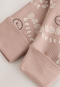 Närbild av ribbad ljusrosa tygärm med vit text och svart smiley-ansiktskontur tryckt på dem.