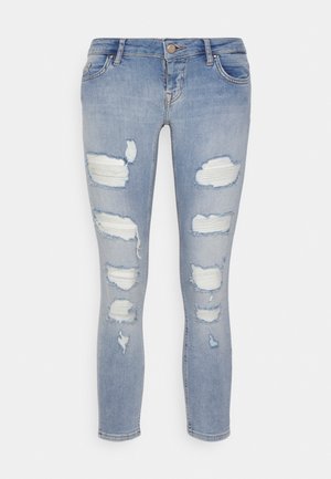 Jeans skinny azzurri chiaro con più toppe orizzontali strappate sulle cosce e sulle ginocchia anteriori, che mostrano un tessuto bianco sottostante.