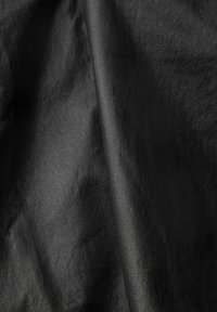 Tissu noir avec des plis doux et une texture lisse et mate visible sous un éclairage doux.