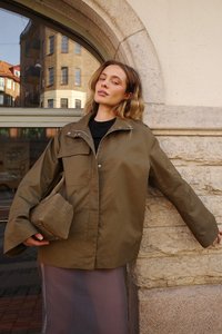 Overdimensioneret olivengrøn jakke med snap-knapper og forlommer, parret med en beige taske. Glat stof og afslappet design.