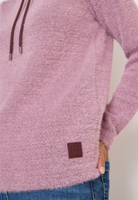 Różowy sweter z dzianiny o teksturowanym wykończeniu, z bordo sznurkiem do ściągania i tkanym metką. Casualowy design z luźnym krojem.