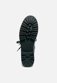 Sole di calzature nera con un motivo di battistrada rugged, caratterizzata da scanalature e tasselli pronunciati per una migliore aderenza. Il materiale sembra essere gomma.