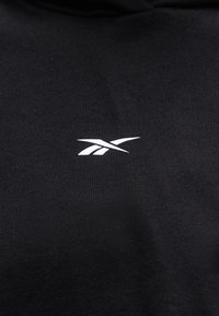 Μαύρο ύφασμα με μικρό λευκό λογότυπο Reebok στο κέντρο της περιοχής του στήθους.