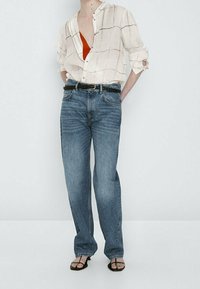 Hvid skjorte med knaplukning og ternet mønster, orange top under, blå lige ben jeans, sort bælte og sorte flade sandaler.