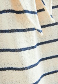 Gestreifter Strickstoff mit einer cremefarbenen Basis und dunkelblauen horizontalen Streifen. Weiche Textur mit lockerem Gewebe und sichtbaren Stichdetails.