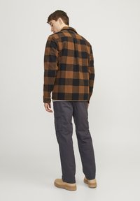 Brun og sort ternet flannelskjorte med krave, båret over grå cargo bukser og beige støvler. Viser struktureret stof og knapdetaljer.
