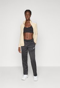 Light beige zip-up jacket, black sports bra, and dark gray joggers. The joggers have an elastic waistband and side pockets. White sneakers.