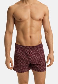 Boxers à motif rouge et marine avec une ceinture élastique, présentant un design géométrique sur un tissu doux. Coupe simple et décontractée.