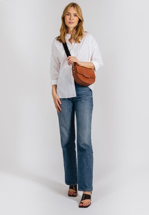 Brun læder crossbody taske med en frontklap, parret med en hvid skjorte med knapper og blå flare jeans, der har sorte hæle sandaler.